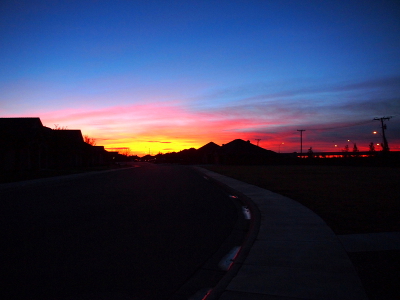 [At the juncture of the dark buildings at the bottom is a very yellow section of sky. Just above it is a pink-red section which contrasts with the blue sky above.]